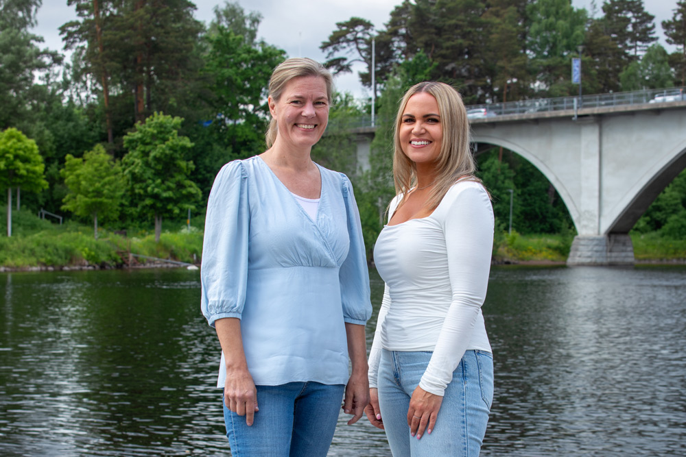 Två anställda står vid vattnet med en bro bakom